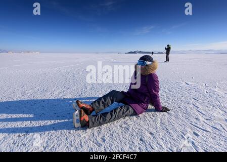 Girl in a skates for skating on ice sitting on the ice and ties it up Stock Photo