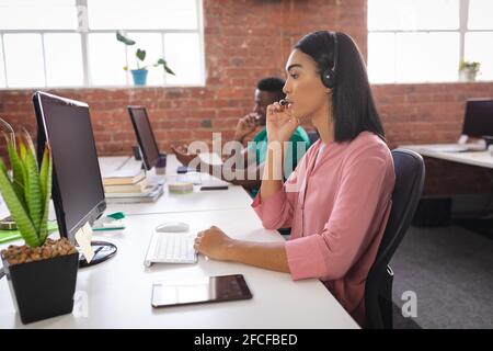 Diverse male and female colleagues having video call sitting in front of computers using headphones Stock Photo