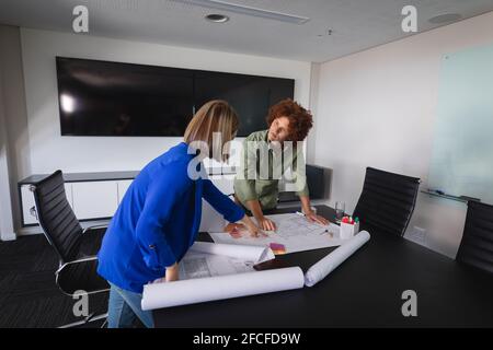 Diverse male and female colleagues in office discussing over blueprint document Stock Photo