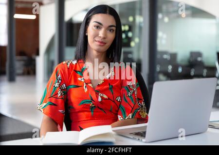 Portrait of smiling mixed race businesswoman sitting in front of laptop Stock Photo