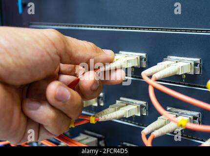 Technician connect fiber cable network to switch port in server room, Concept internet network management Stock Photo