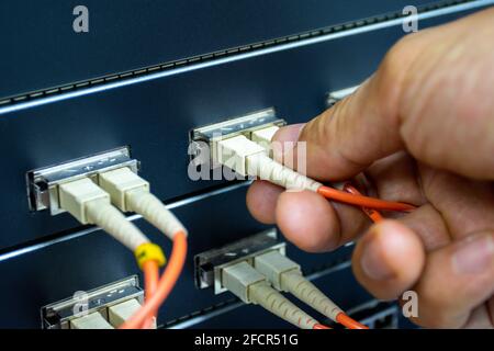 Technician connect fiber cable network to switch port in server room, Concept internet network management Stock Photo