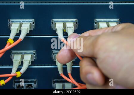 Technician connect fiber cable network to switch port in server room, Concept internet network management Stock Photo
