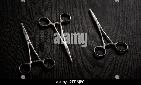 Hemostatic Forceps scissors on top of the dark wooden tabletop. Stock Photo