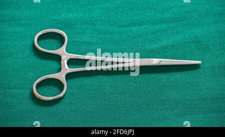 Isolated Hemostatic Forceps scissor on a green-clothed tabletop. Stock Photo