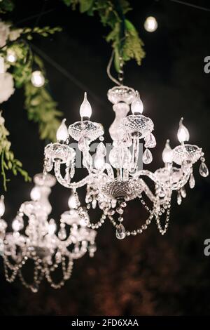 Crystal clear chandeliers with candlesticks and candelabra, candle light bulbs, glass pendants and crystals. In the dark on black. background at night Stock Photo