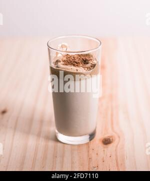 Homemade Dalgona coffee glass in a wooden textured tabletop. whisked instant coffee topping and fresh milk in the bottom making the delicious Korean d Stock Photo