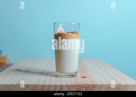 Homemade Dalgona coffee glass in a wooden textured tabletop. whisked instant coffee topping with fresh milk, making the delicious Korean drink. Trendy Stock Photo