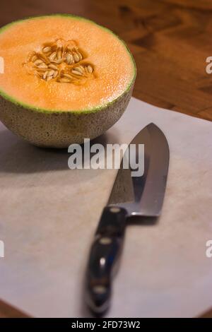 half cantaloupe with seeds on cutting board with knife Stock Photo