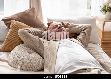 Senior hispanic man resting at home sleeping on bed. Grandfather having a nap. Stock Photo