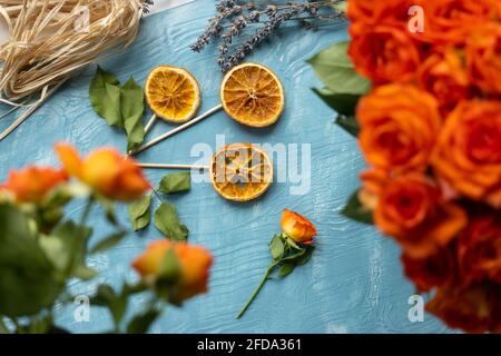 A flower made from dried orange slices with orange rose blossoms with lavender on blue wooden background Stock Photo