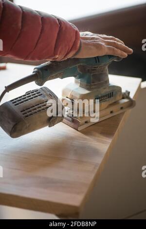 Man sanding wood plank using electric sand machine. Stock Photo