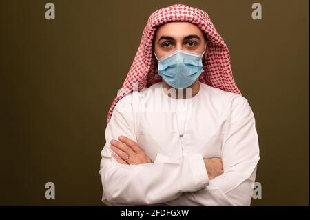 Muslim man wearing a medical mask. Portrait of a young arab man in traditional dress.  Stock Photo
