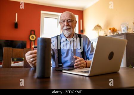 Senior man using Virtual Assistant at home Stock Photo