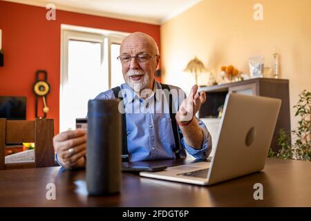 Senior man using Virtual Assistant at home Stock Photo