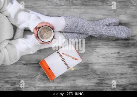 A comforting cup of coffee in the hands of a woman with a notebook for work Stock Photo