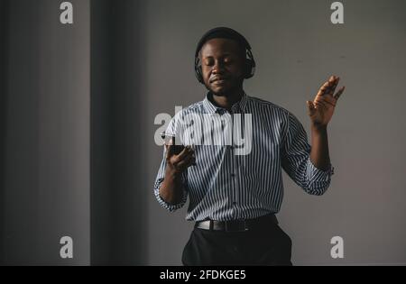 Handsome Afro American businessman in casual clothes and headphones is listening to music using a smart phone Stock Photo