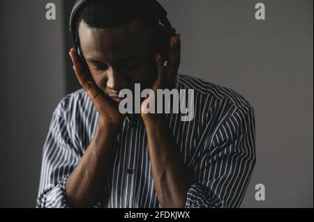 Handsome Afro American businessman in casual clothes and headphones is listening to music using a smart phone Stock Photo