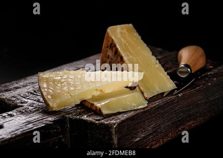 Close-up of Cheddar cheese. Semi-soft aged cow's milk cheese according to an old English recipe. Piece of cheese on a dark wooden board and knife for Stock Photo