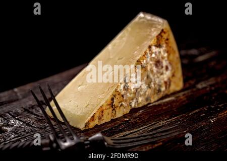 Close-up of a piece of cheddar cheese. Aged cheese made from farm milk, an old English recipe. A piece of cheese on a dark wooden board and a cheese k Stock Photo