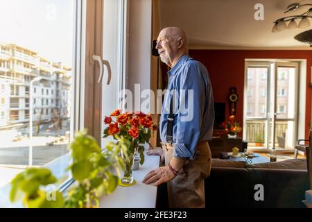Senior Man Looking Through Window at Home Stock Photo