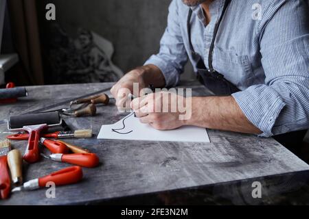 Beautiful bearded brunette craftsman in apron and eyeglasses making sketch using felt pen. Linocut professional artist handmade worker. High quality photo Stock Photo