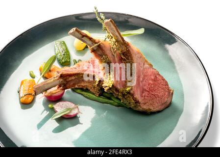 Crusted lamb ribs cutlets with bone in green dish with carrot, radishes and courgette, close up Stock Photo