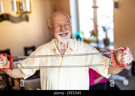 Senior man exercising using chest expander in living room Stock Photo