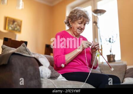 Senior woman sitting on sofa at home knitting Stock Photo