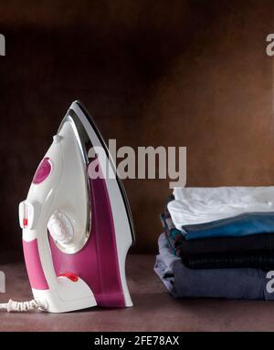 pink electric iron and a stack of ironed clothes on an ironing