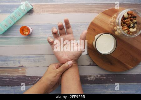 man suffering pain in hand with medical pills , milk and almond nut on table  Stock Photo