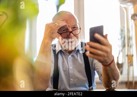Shot of a senior man using a mobile phone at home Stock Photo