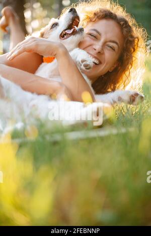 Smiling woman playing in green grass with a dog. Stock Photo