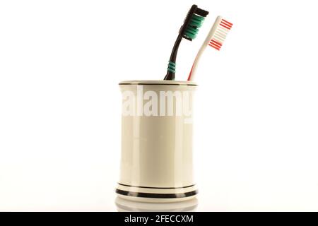 Two toothbrushes in a light ceramic glass on a white background. Stock Photo