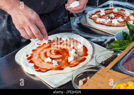 Margherita Pizza being made at food market, putting on mozzarella cheese, close up. Stock Photo