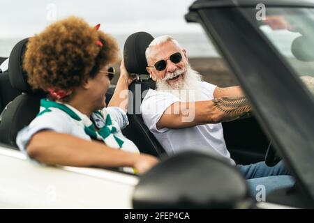 Happy senior couple having fun driving on new convertible car - Mature people enjoying time together during road trip tour vacation Stock Photo