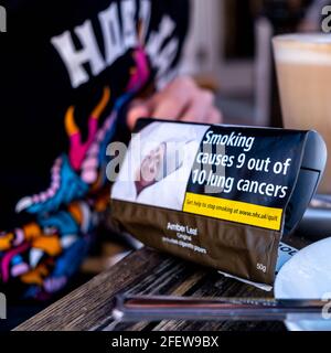 Epsom Surrey, London England UK, April 23 2021, Packet Of Rolling Cigarette Tobacco Next To A Latte Coffee On A Table Top Stock Photo