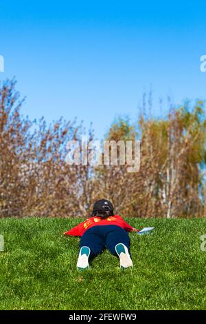 Young woman laying on her stomach on grass and reading a book in Steveston British Columbia Canada Stock Photo