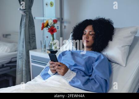 African american female patient lying in hospital bed using smartphone Stock Photo