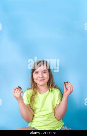 Cute little girl enjoys eating sushi. Cheerful funny caucasian blond preschool child girl with various sushi roll and chopsticks. On bright blue backg Stock Photo