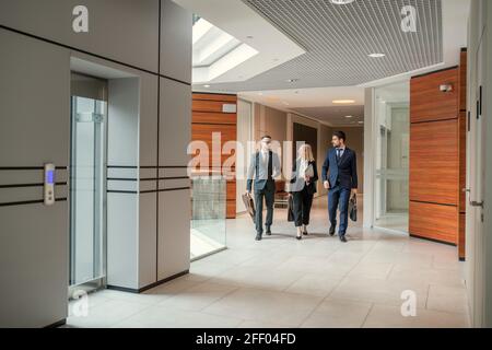 Modern business colleagues of different ages walking in corridor and discussing plan of work day Stock Photo