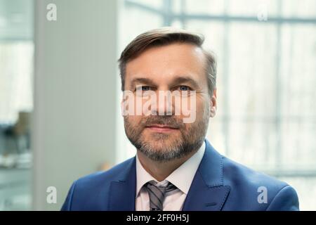 Portrait of smiling handsome middle-aged businessman with stubble standing in contemporary office Stock Photo