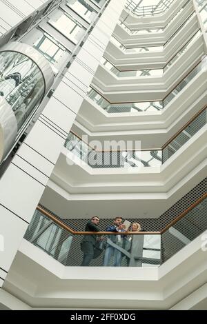 Below view of concentrated business people standing at railing and analyzing online document on tablet in modern office center Stock Photo