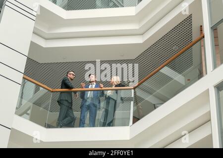 Below view of colleagues of lawyers standing at railing and discussing line of defense in corridor Stock Photo