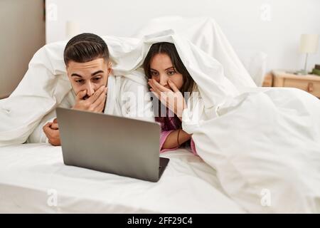 Young hispanic couple watching movie using laptop lying in bed. Stock Photo