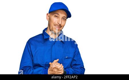 Bald man with beard wearing builder jumpsuit uniform with hands together and crossed fingers smiling relaxed and cheerful. success and optimistic Stock Photo