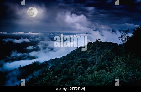 Landscape at national park. Peaks of hills are sticking out from foggy background, fresh green nature against beautiful sky and full moon. The moon ta Stock Photo