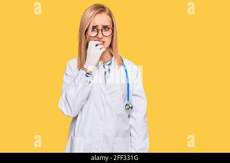 Beautiful caucasian woman wearing doctor uniform and stethoscope looking stressed and nervous with hands on mouth biting nails. anxiety problem. Stock Photo