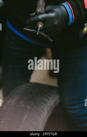 Mechanic in a workshop standing over a car tire, holding a screwdriver Stock Photo