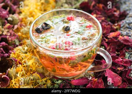Glass cup of healthy tea with medicinal herbs and healthy berries. Dried echinacea, calendula, wild marjoram, rose petals on table. Alternative medici Stock Photo